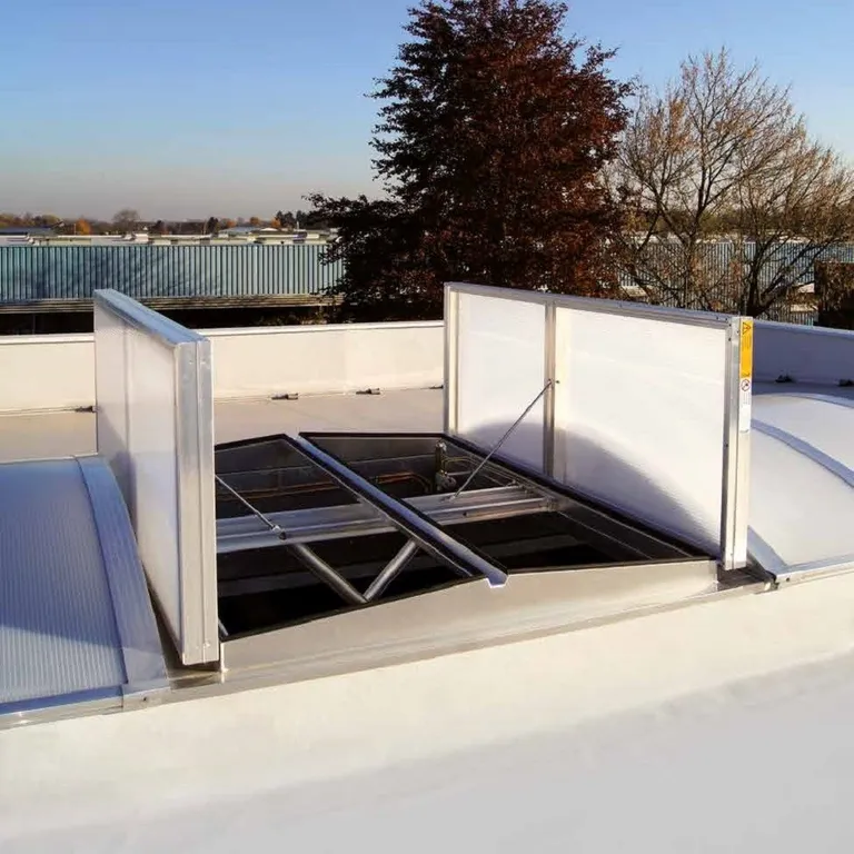 Open roof ventilation hatch on a flat rooftop, surrounded by trees and industrial buildings in the background under a clear sky.