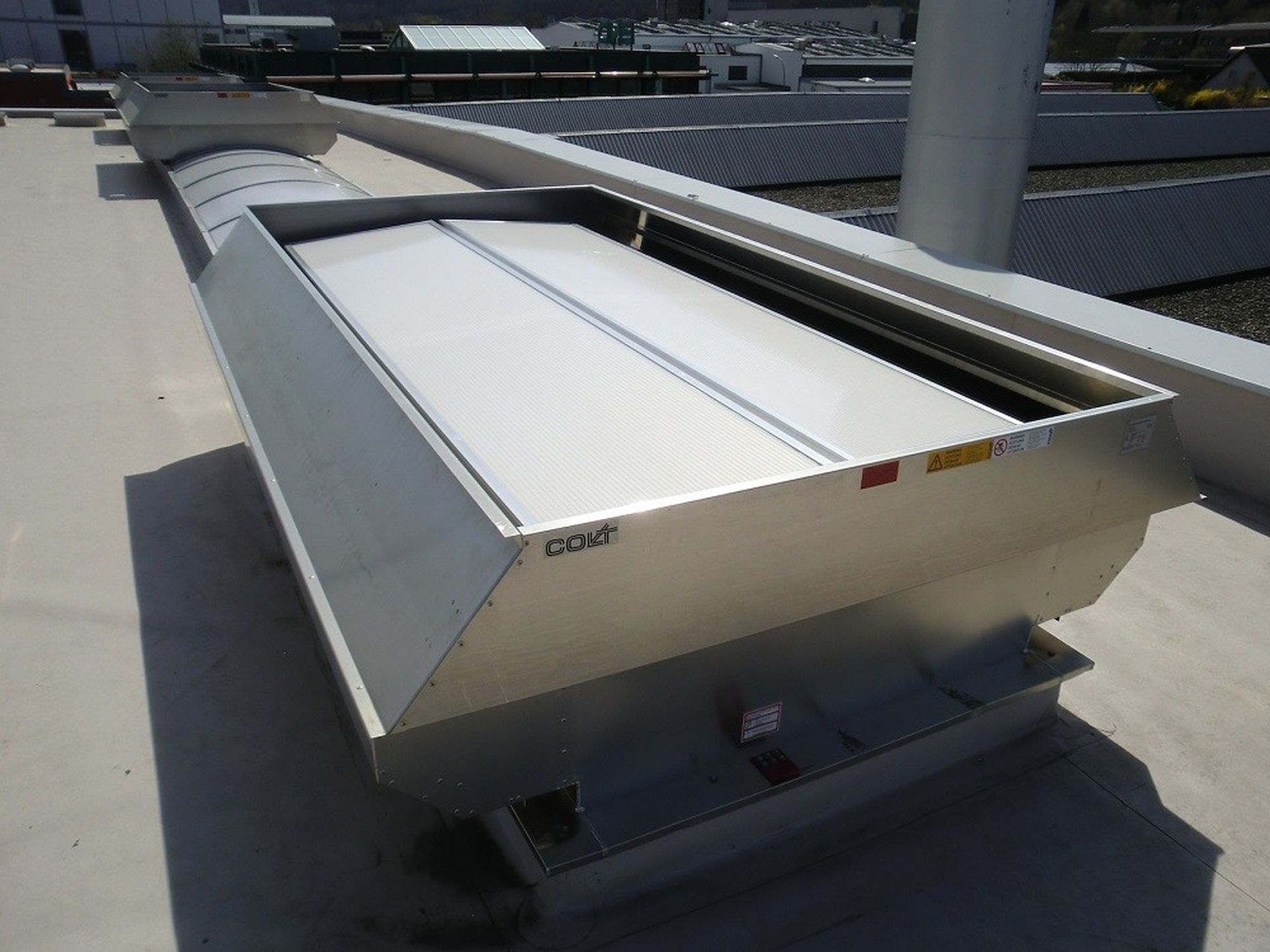 Industrial rooftop ventilation system with metal casing and a white cover, situated on a flat surface under a sunny sky.