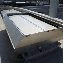 Industrial rooftop ventilation system with metal casing and a white cover, situated on a flat surface under a sunny sky.