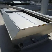 Industrial rooftop ventilation system with metal casing and a white cover, situated on a flat surface under a sunny sky.