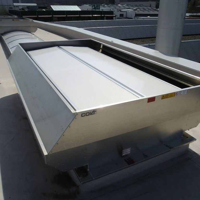 Industrial rooftop ventilation system with metal casing and a white cover, situated on a flat surface under a sunny sky.