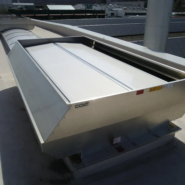 Industrial rooftop ventilation system with metal casing and a white cover, situated on a flat surface under a sunny sky.