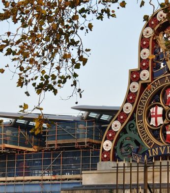 Ornate railway emblem with historical symbols and "London Chatham and Dover Railway" text, framed by autumn branches against a building backdrop.