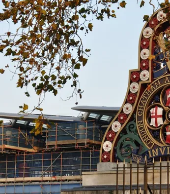 Ornate railway emblem with historical symbols and "London Chatham and Dover Railway" text, framed by autumn branches against a building backdrop.