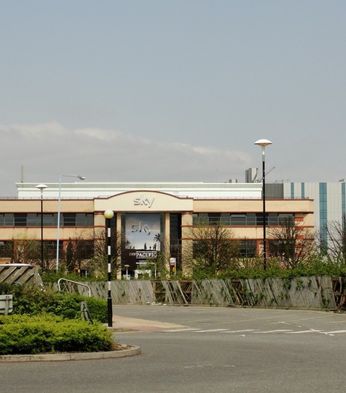A large office building with "Sky" signage, surrounded by trees and a parking area, set against a clear sky.