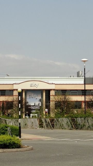 A large office building with "Sky" signage, surrounded by trees and a parking area, set against a clear sky.
