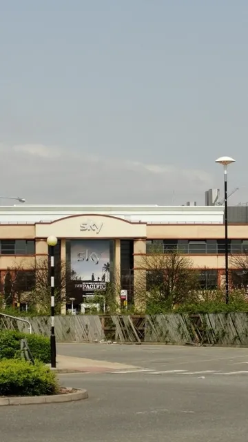 A large office building with "Sky" signage, surrounded by trees and a parking area, set against a clear sky.