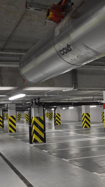 Underground parking garage with empty spaces, marked lanes, and black-and-yellow striped columns under fluorescent lighting.
