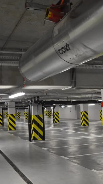 Underground parking garage with empty spaces, marked lanes, and black-and-yellow striped columns under fluorescent lighting.