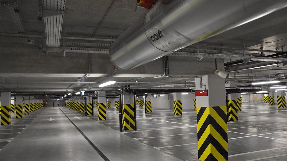 Underground parking garage with empty spaces, marked lanes, and black-and-yellow striped columns under fluorescent lighting.