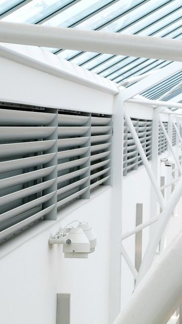 Interior view of a modern shopping centre, showcasing structural beams and louvered panels, with a glimpse of the shops below.