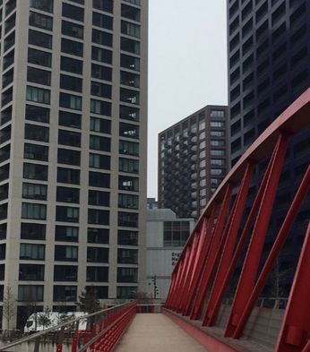 Red pedestrian bridge leading to tall modern residential buildings in London, under an overcast sky.