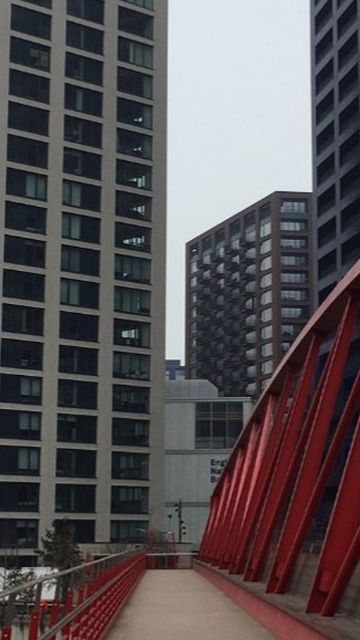 Red pedestrian bridge leading to tall modern residential buildings in London, under an overcast sky.