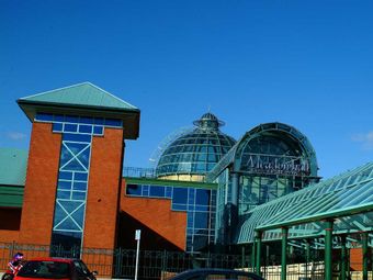 Modern shopping center building with red brick and glass dome, clear blue sky in the background.