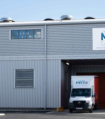 A white van with "MRT Castings" branding is parked in a large, industrial grey building with the same company logo on the facade.