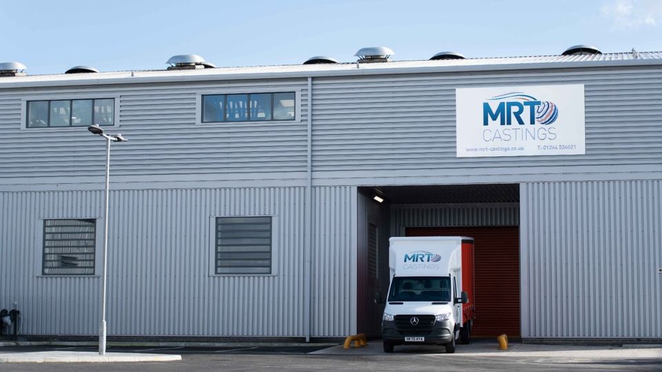 A white van with "MRT Castings" branding is parked in a large, industrial grey building with the same company logo on the facade.
