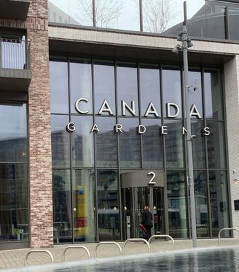 Glass entrance of residential Canada Gardens building with "2" displayed over the door, featuring large windows and brick facade.