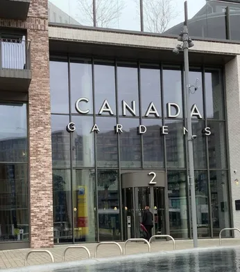 Glass entrance of residential Canada Gardens building with "2" displayed over the door, featuring large windows and brick facade.
