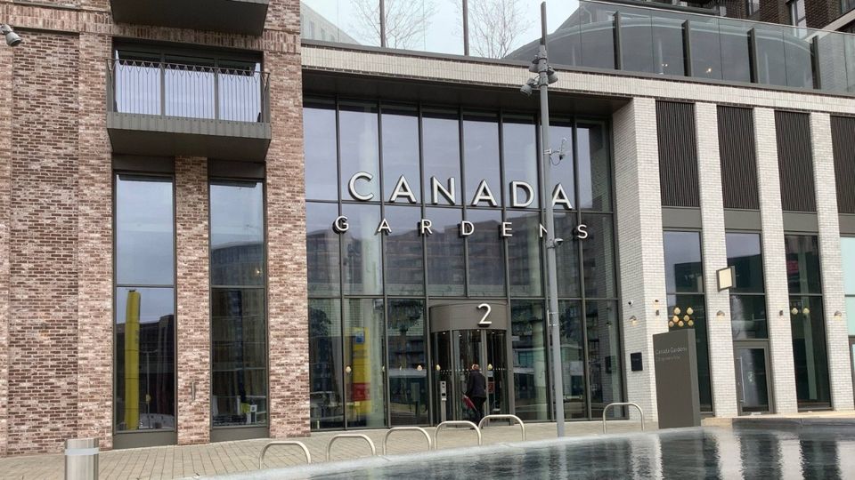 Glass entrance of residential Canada Gardens building with "2" displayed over the door, featuring large windows and brick facade.