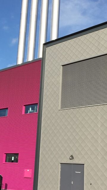 Modern industrial building with gray and pink facades, featuring louvre and multiple chimneys against a clear blue sky.