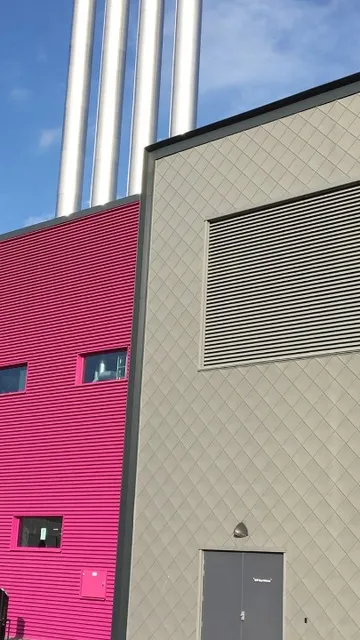 Modern industrial building with gray and pink facades, featuring louvre and multiple chimneys against a clear blue sky.
