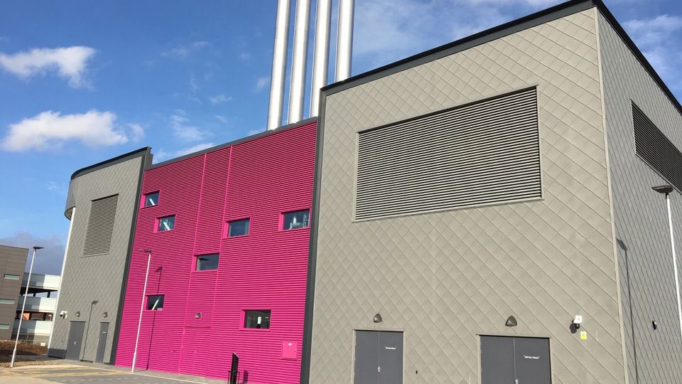 Modern industrial building with gray and pink facades, featuring louvre and multiple chimneys against a clear blue sky.