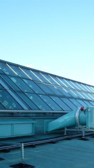 Rooftop view showcasing a slanted glass facade and a large dome skylight with visible smoke ventilator systems under a clear blue sky.
