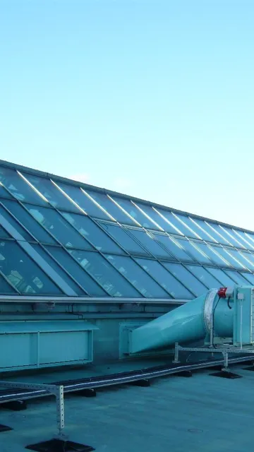 Rooftop view showcasing a slanted glass facade and a large dome skylight with visible smoke ventilator systems under a clear blue sky.