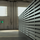 Interior of an industrial warehouse with large metal louvered panels on the right and bright windows in the background.