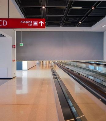 Empty airport terminal with a smoke curtain. Features include a moving walkway, red signs indicating exits and gates A01-36, a large "7" on the wall, and a trash bin in the corner.