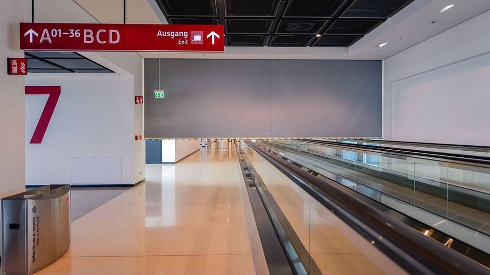 Empty airport terminal with a smoke curtain. Features include a moving walkway, red signs indicating exits and gates A01-36, a large "7" on the wall, and a trash bin in the corner.
