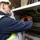 An electrician in a safety vest and helmet uses a multimeter to check wires inside an electrical panel.