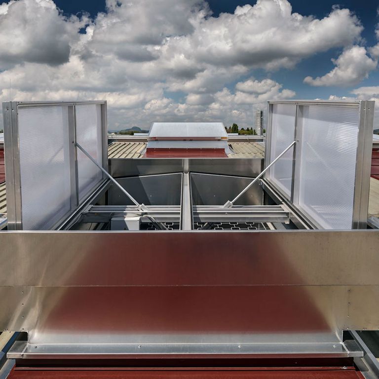 A rooftop smoke ventilation system with open vents, set against a cloudy sky background.