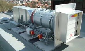 Industrial rooftop ventilation unit with a cylindrical metal duct and square outlets, overlooking city buildings in the background.