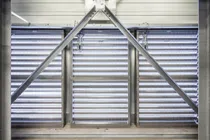 Metallic structure with diagonal beams and horizontal louvered panels, allowing light through, creating an industrial appearance.