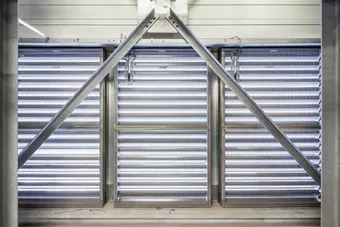 Metallic structure with diagonal beams and horizontal louvered panels, allowing light through, creating an industrial appearance.