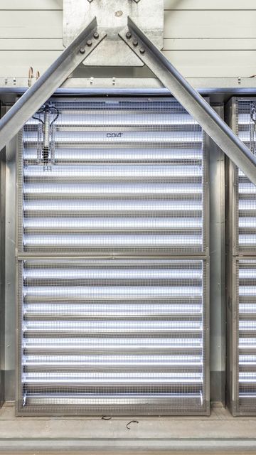 Metallic structure with diagonal beams and horizontal louvered panels, allowing light through, creating an industrial appearance.