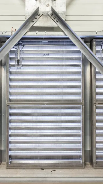 Metallic structure with diagonal beams and horizontal louvered panels, allowing light through, creating an industrial appearance.