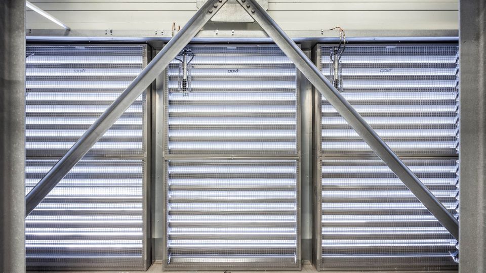 Metallic structure with diagonal beams and horizontal louvered panels, allowing light through, creating an industrial appearance.