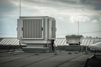 Rooftop HVAC unit on a flat industrial roof with cloudy sky in the background.