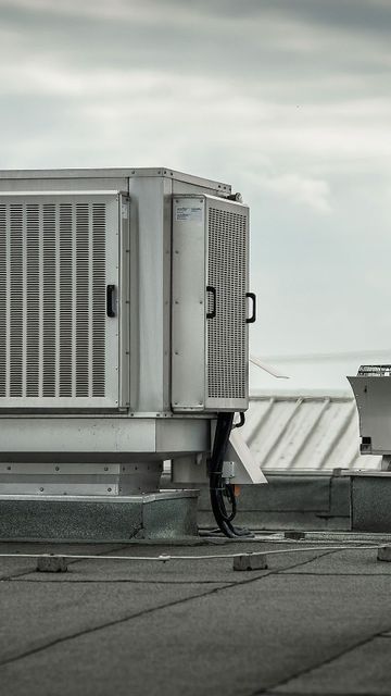 Rooftop HVAC unit on a flat industrial roof with cloudy sky in the background.