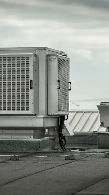 Rooftop HVAC unit on a flat industrial roof with cloudy sky in the background.