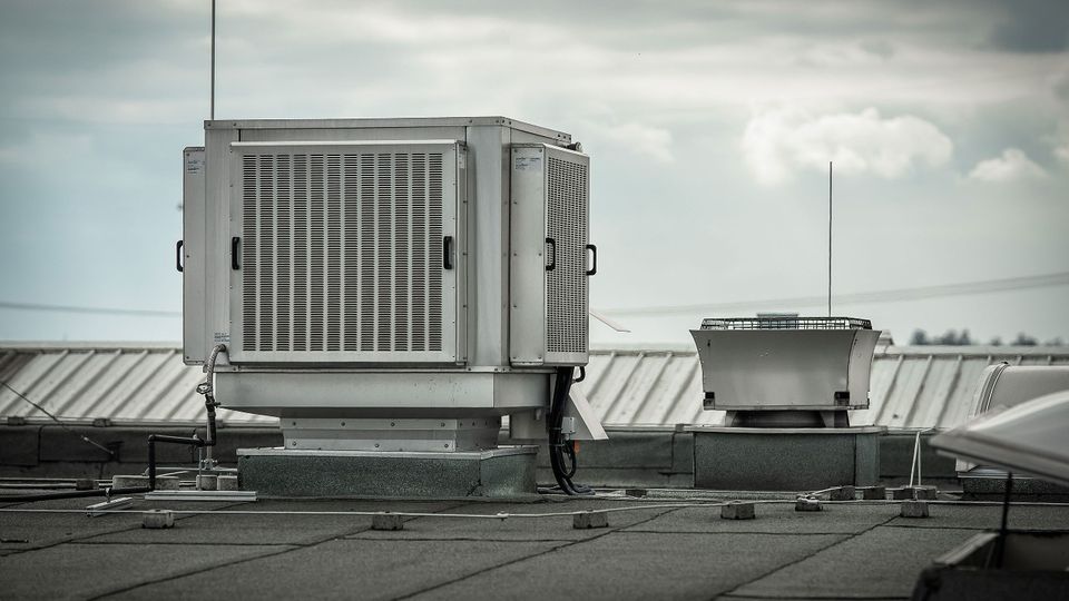 Rooftop HVAC unit on a flat industrial roof with cloudy sky in the background.