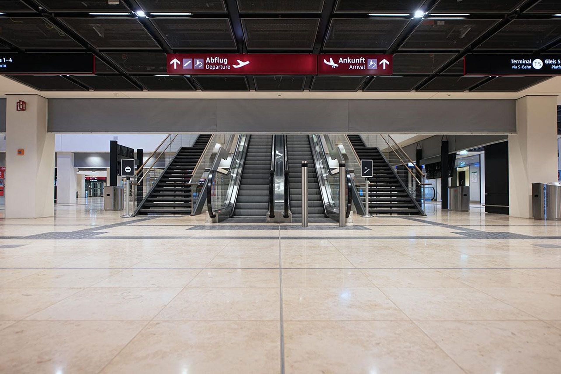 Sleek airport interior with escalators and stairs under signs for departures and arrivals in multiple languages. A Smokemaster SM5 is installed above the escalator.