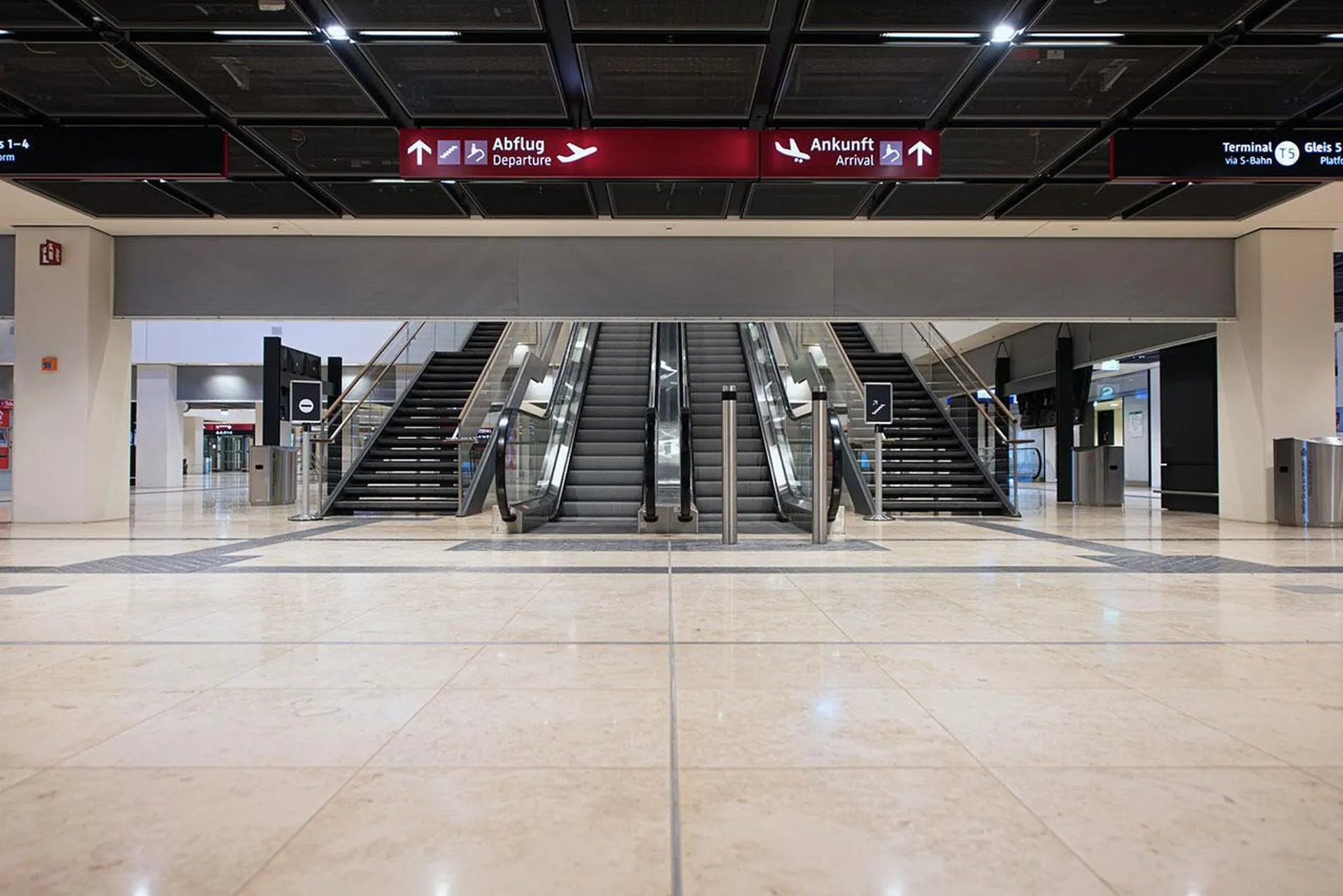 Sleek airport interior with escalators and stairs under signs for departures and arrivals in multiple languages. A Smokemaster SM5 is installed above the escalator.
