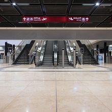 Sleek airport interior with escalators and stairs under signs for departures and arrivals in multiple languages. A Smokemaster SM5 is installed above the escalator.