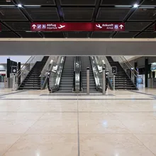 Sleek airport interior with escalators and stairs under signs for departures and arrivals in multiple languages. A Smokemaster SM5 is installed above the escalator.