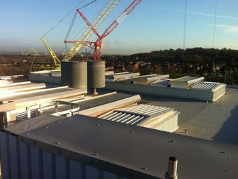 Rooftop of Ineos Waste to Energy Plant, with natural ventilation and louvre systems on the roof, overlooking a cityscape with cranes in the background.