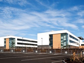 Modern two-story office buildings with large windows, surrounded by an empty parking lot under a clear blue sky.