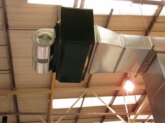 Industrial heating system mounted on a warehouse ceiling with metal ducts and a large fan unit.